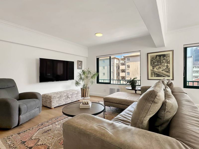 A bright and well-maintained living room featuring crown molding, recessed lighting, and large sliding windows with views of the surrounding apartment complex.