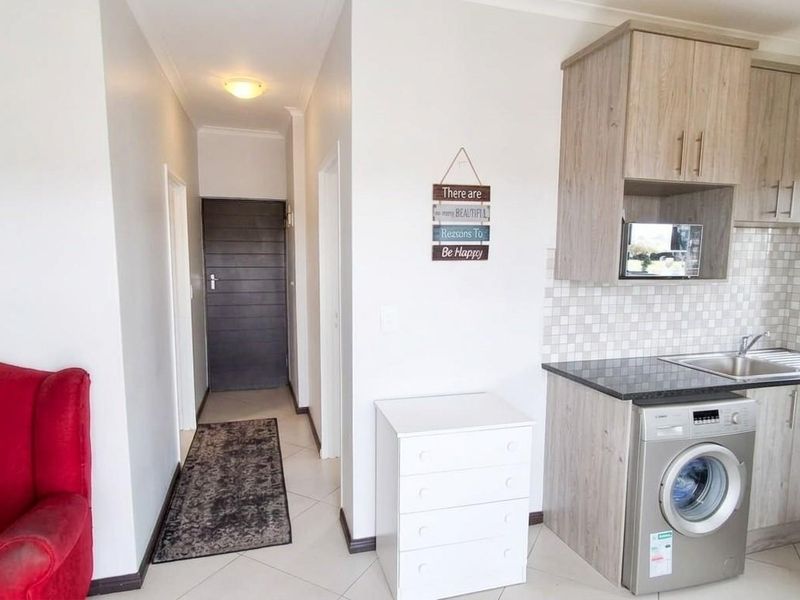 Open plan kitchen area featuring modern wood-look cabinetry, dark laminate countertops, and tiled flooring, seamlessly connected to the apartment entrance hallway.