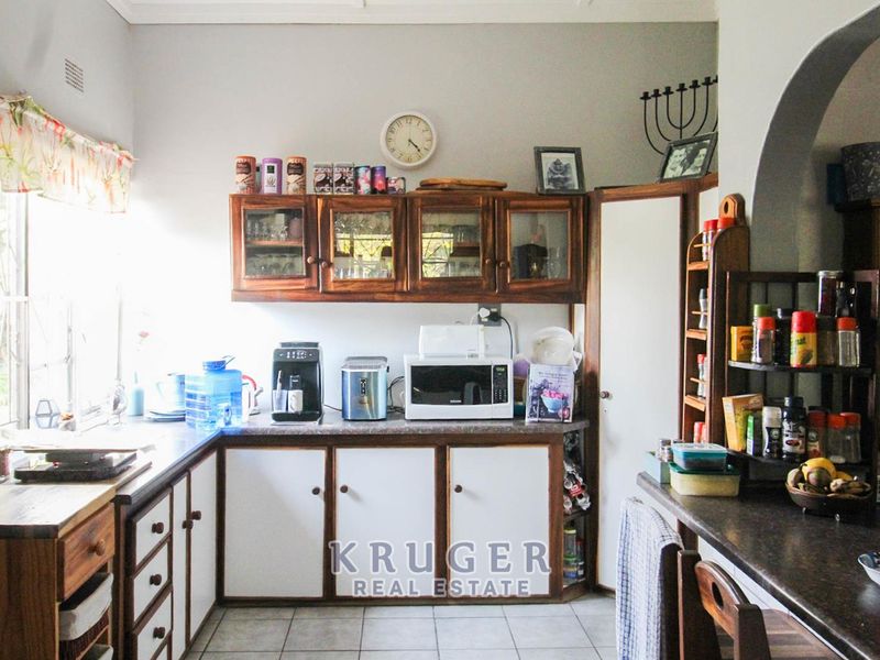 A functional kitchen featuring wooden cabinetry, laminate countertops, and tiled flooring, with an open archway leading to adjacent living spaces.