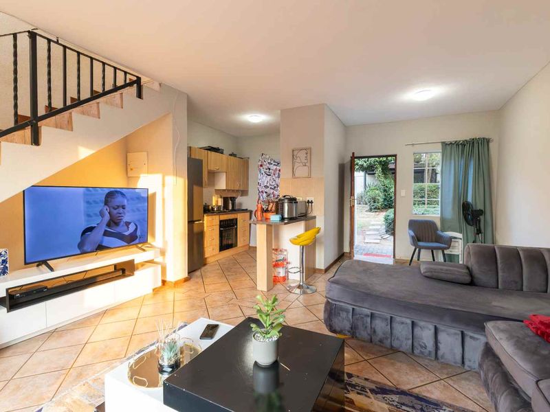 Open-plan living area featuring tiled floors, a compact kitchen with built-in cabinetry, and a staircase leading to the upper level.