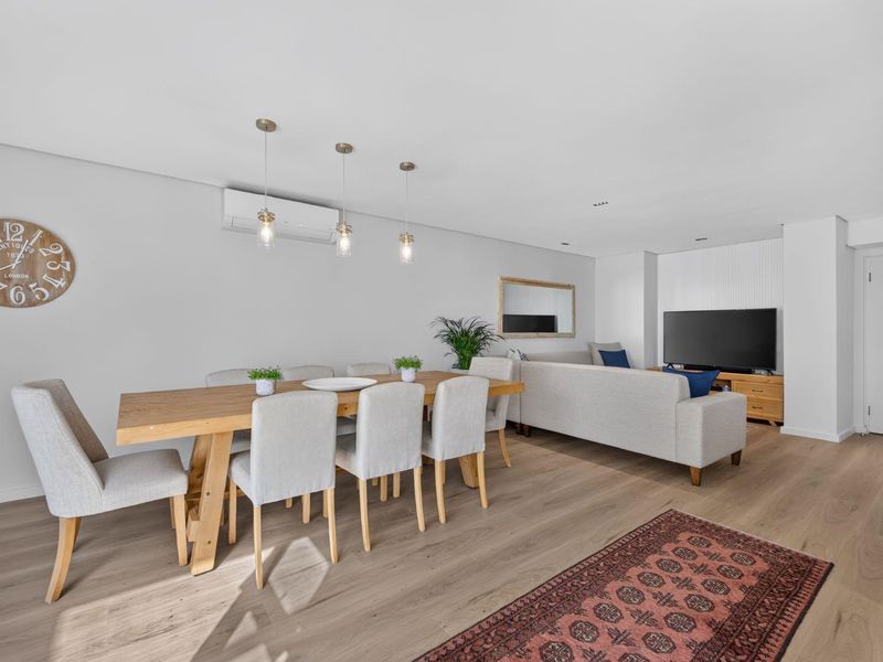 Spacious open-plan living and dining area featuring light timber flooring, modern pendant lighting, and a wall-mounted air conditioning unit.