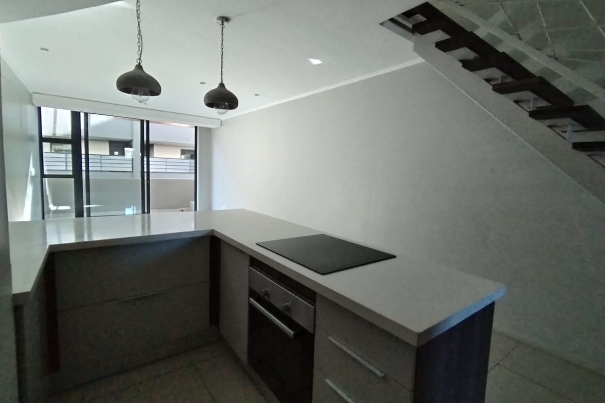 Modern kitchen featuring stone countertops, built-in oven, electric hob, and sleek cabinetry, situated beneath an open staircase with access to an outdoor area.