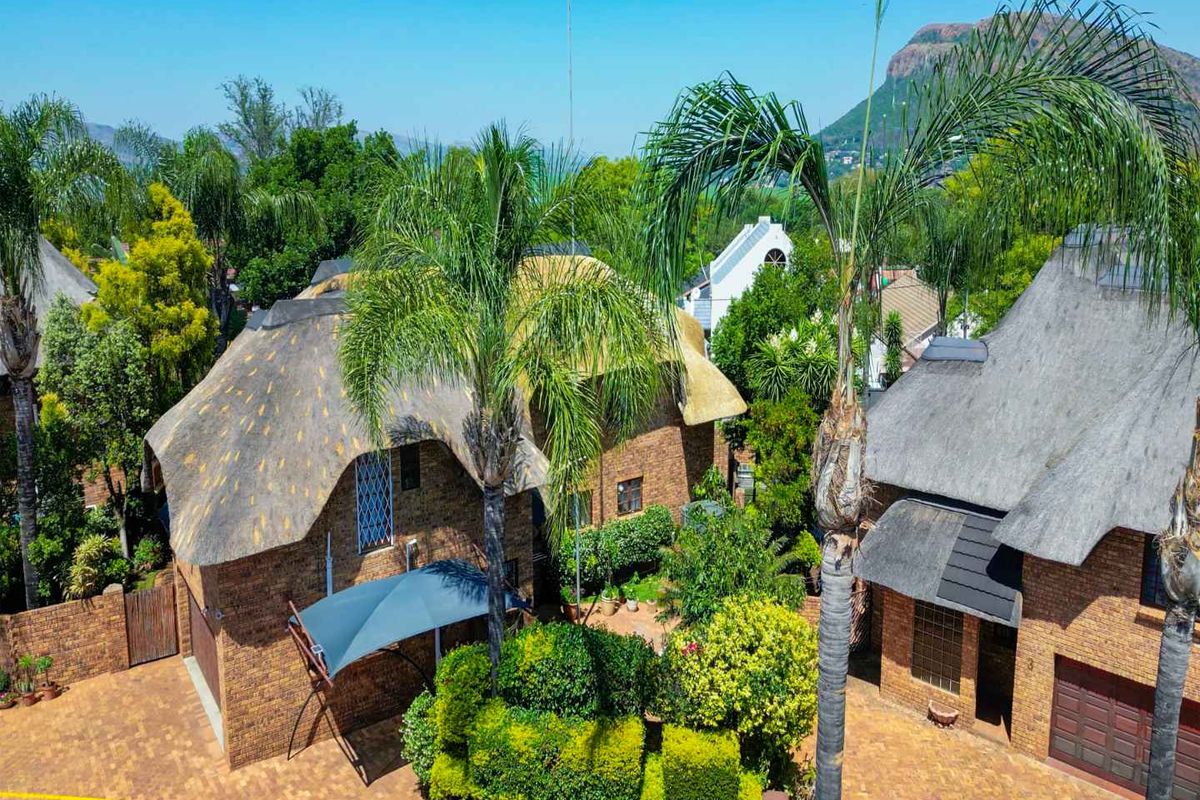 Aerial view of a residential property featuring traditional thatched roof architecture, brick facade, paved driveway, and established garden landscaping.