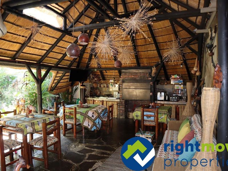Spacious outdoor entertainment area featuring a traditional thatched roof, exposed timber beams, stone flooring, and a built-in brick braai facility.