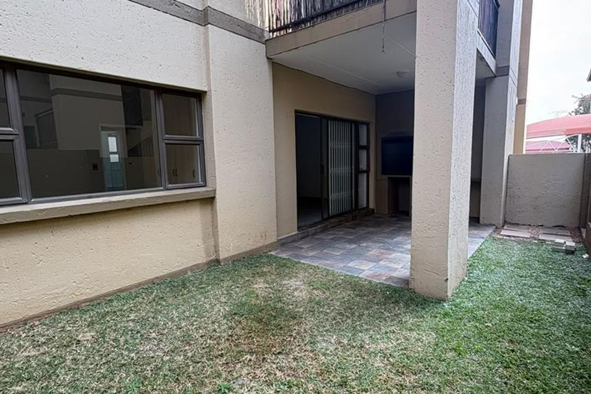 Rear exterior view of the apartment featuring a private garden, a tiled patio with a built-in braai, and an upper-level balcony.
