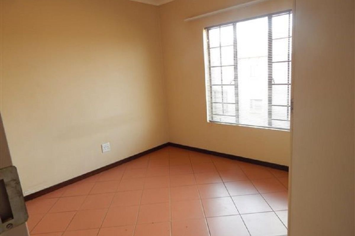 A vacant bedroom featuring tiled flooring and a window with fitted blinds, offering a neutral canvas for personalization.