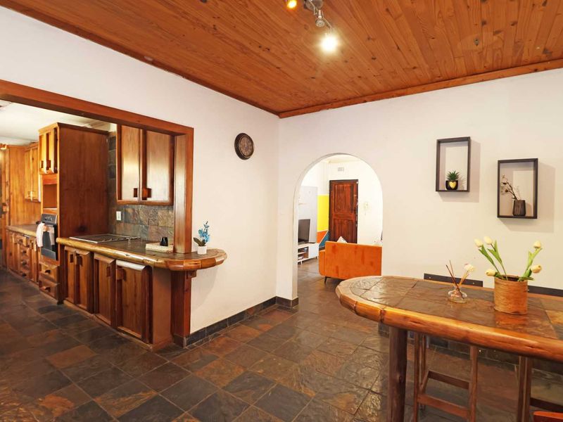 Open plan kitchen and dining area featuring rustic timber ceilings, slate tile flooring, and custom wooden cabinetry with a stone backsplash.