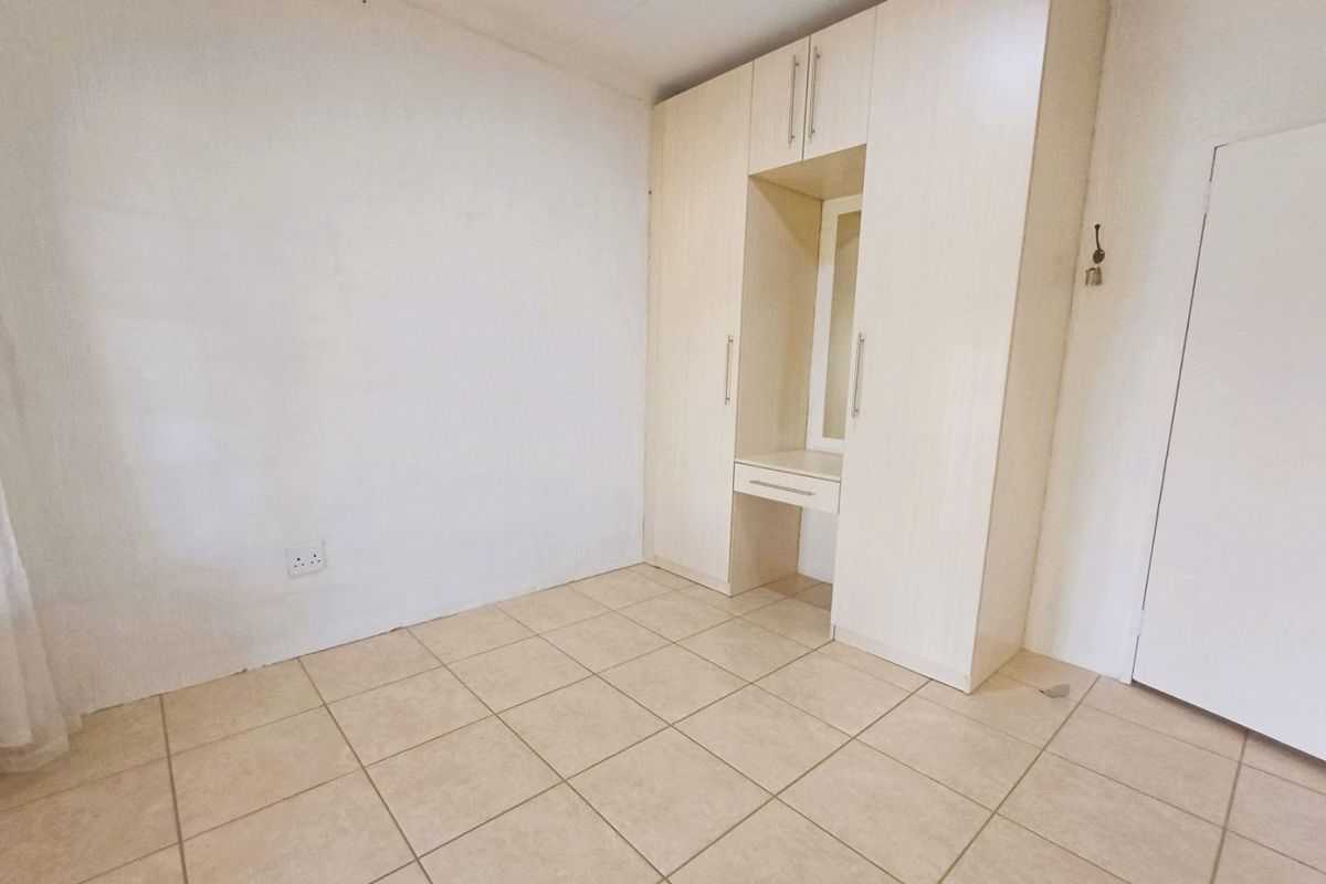 A clean, empty bedroom featuring neutral tiled flooring and a built-in wardrobe with an integrated vanity area.