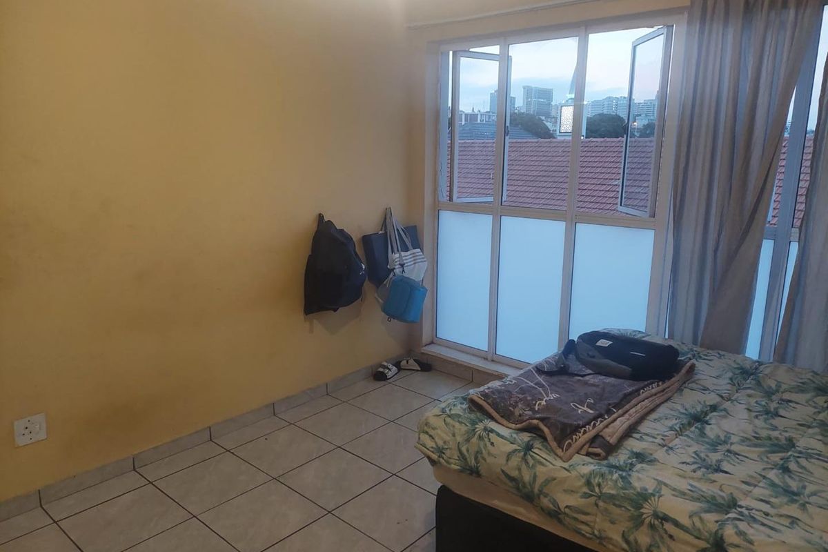 A bedroom featuring tiled flooring and large aluminium-framed windows with frosted glass panels, offering natural light and an urban view.