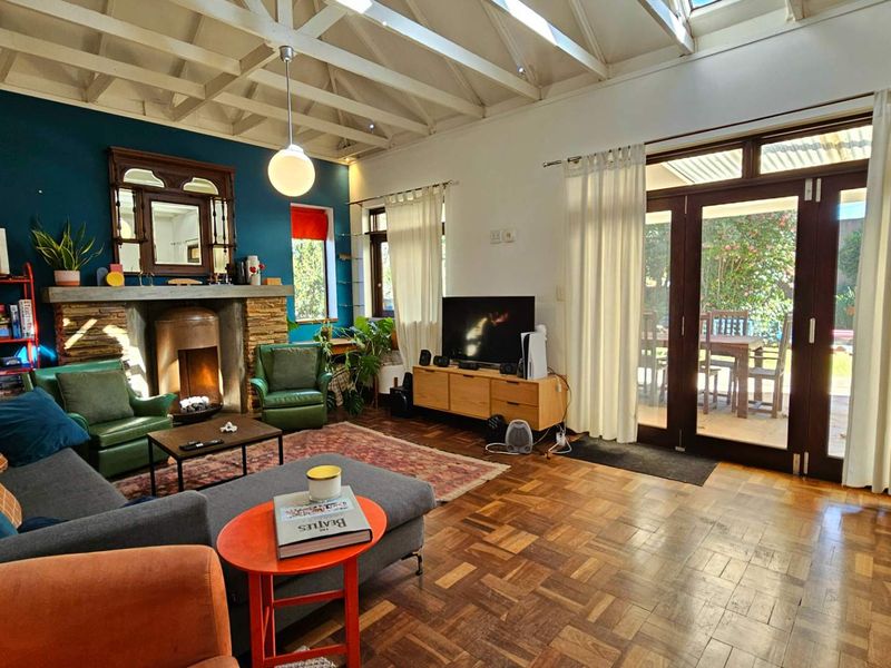 Spacious living room featuring a stone-clad fireplace, exposed timber beam ceiling with skylights, and classic parquet flooring, with direct access to the patio.