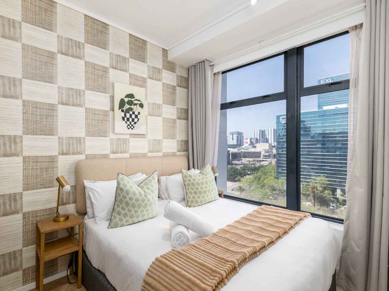 A well-lit bedroom featuring textured wallpaper and large floor-to-ceiling windows offering an expansive urban view.