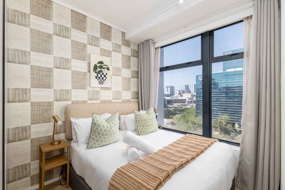 A well-lit bedroom featuring textured wallpaper and large floor-to-ceiling windows offering an expansive urban view.