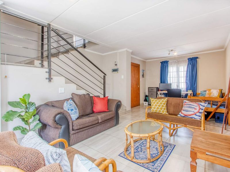 A spacious living area featuring tiled flooring and an open-plan staircase with a modern metal balustrade.