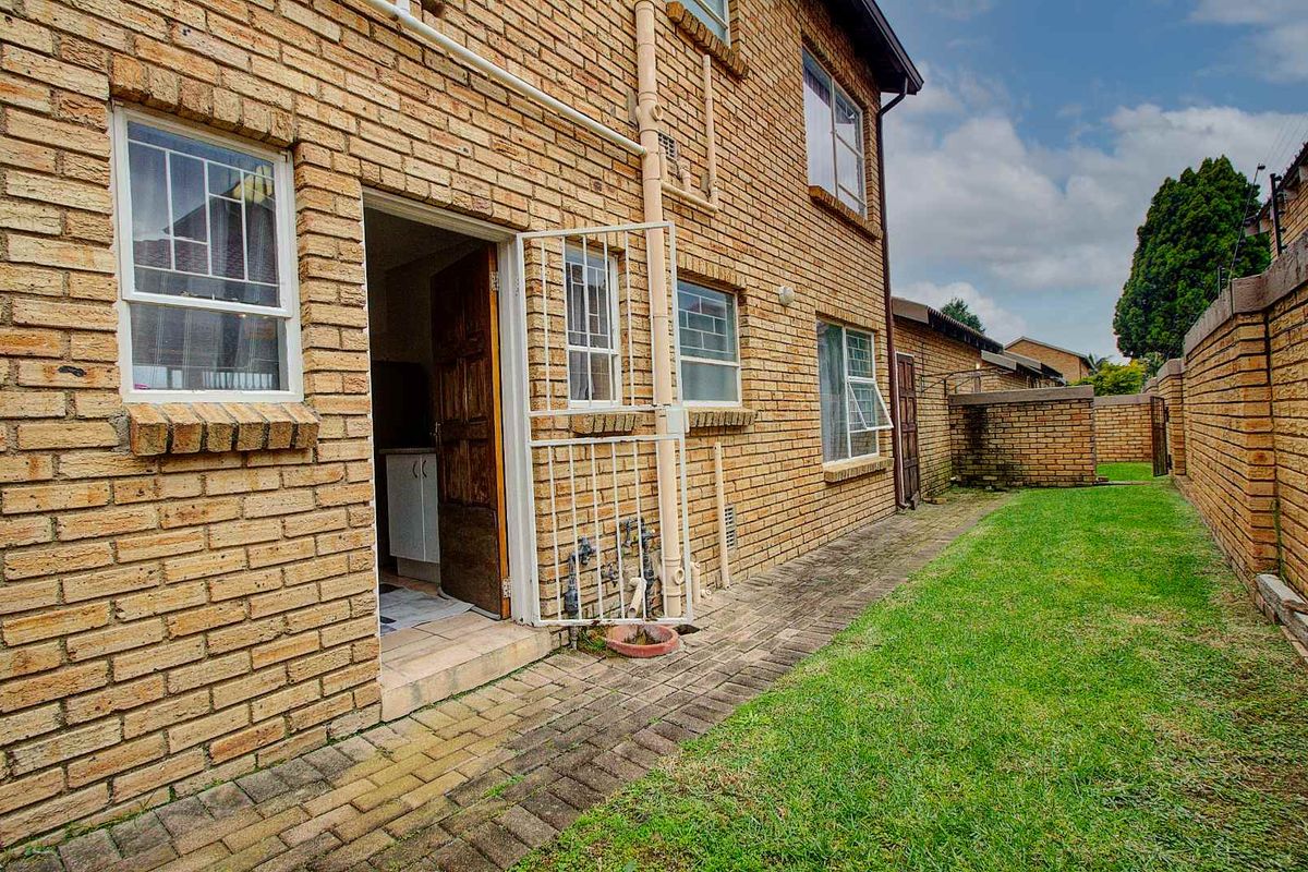 Exterior view of the townhouse rear facade featuring face-brick construction, a paved walkway, and a small private garden area.