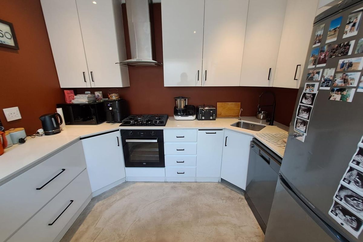 Modern kitchen featuring white cabinetry, contrasting dark red walls, built-in gas hob, oven, extractor fan, and integrated dishwasher.