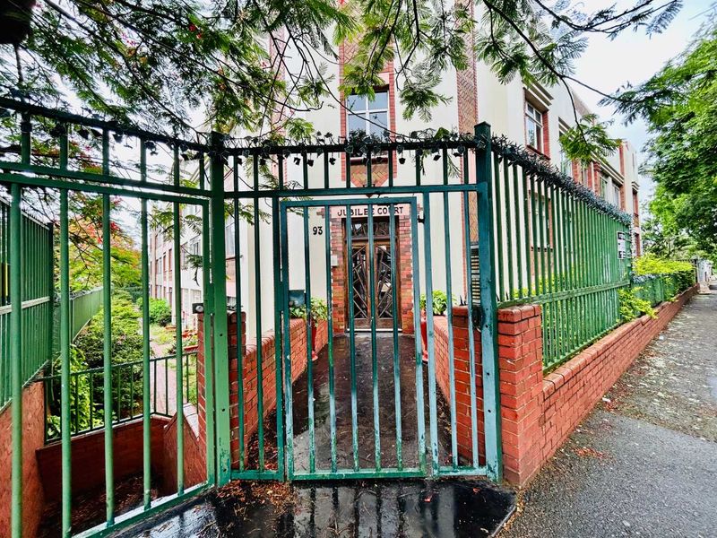 Front entrance view of Jubilee Court apartment building featuring a gated security perimeter and brick boundary wall.