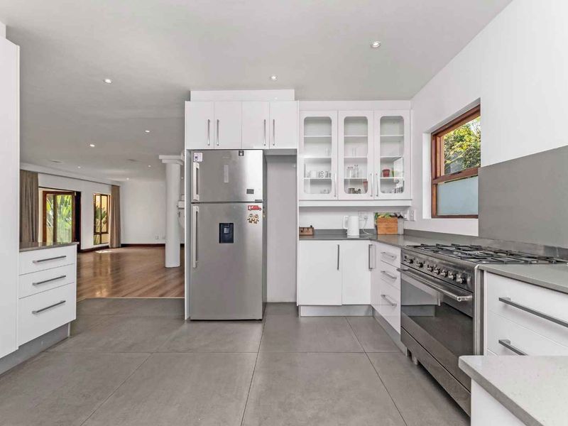 Modern open-plan kitchen featuring sleek white cabinetry, stone countertops, a gas stove, and tiled flooring, flowing seamlessly into the adjacent living area.