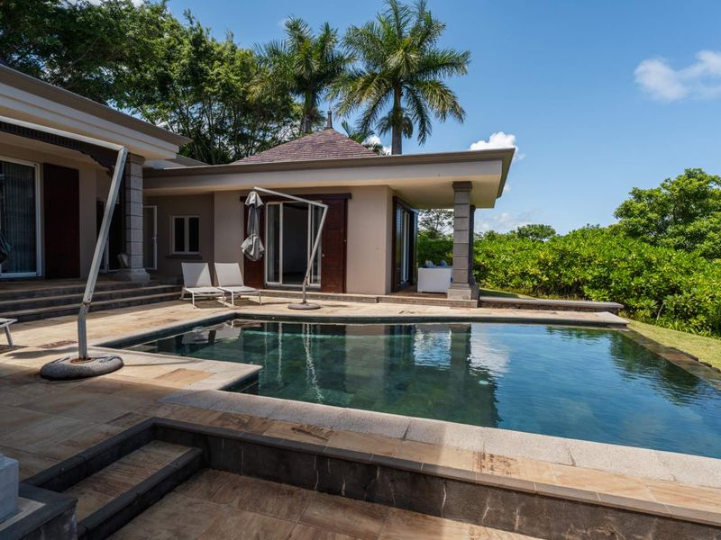 A well-maintained outdoor pool area featuring stone paving, a built-in swimming pool, and covered patio space, set within a landscaped garden environment.