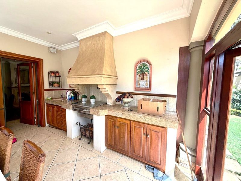 Covered patio area featuring a built-in braai with a stone-clad extractor hood, granite countertops, and wooden cabinetry, overlooking the garden.