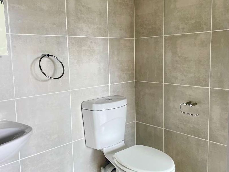 A clean, modern bathroom featuring neutral wall and floor tiles, a white toilet, and a wall-mounted washbasin.