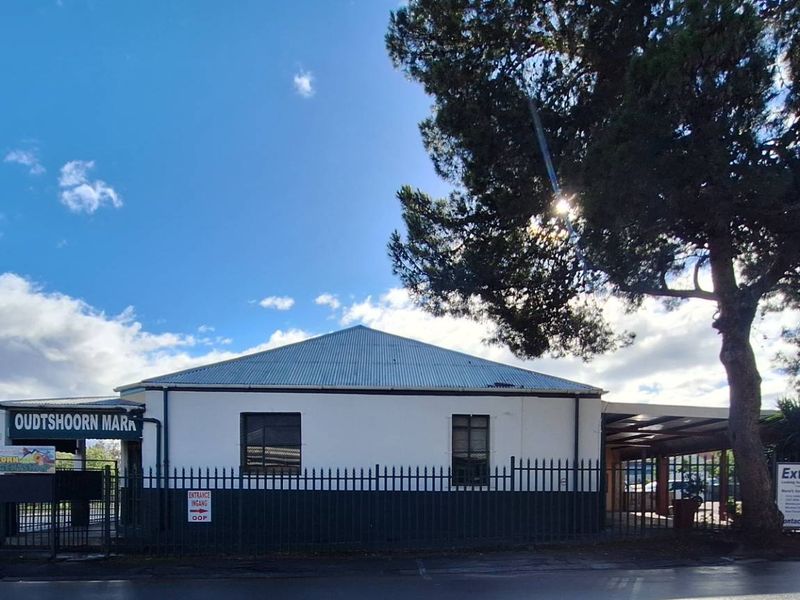 Front exterior view of a commercial industrial building featuring a metal roof, security fencing, and prominent signage.