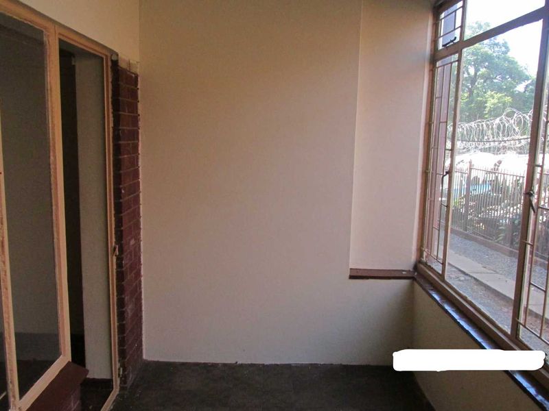 An enclosed balcony or sunroom featuring large windows with security bars, exposed brick accents, and concrete flooring, offering a blank canvas for renovation.