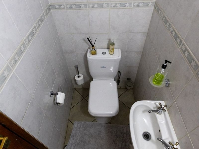 A compact guest bathroom featuring a white toilet, wall-mounted basin, and neutral ceramic tiling throughout.