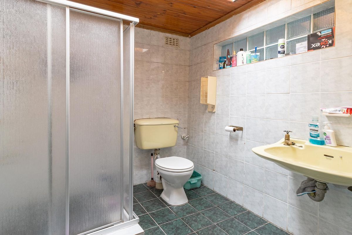 A dated bathroom featuring a shower enclosure, toilet, and washbasin, complemented by a timber ceiling and glass block window detail.