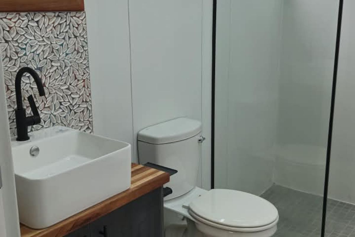 Modern bathroom featuring a vessel sink with black fixtures, a wooden vanity, mosaic backsplash, and a walk-in shower with a black-framed glass screen.