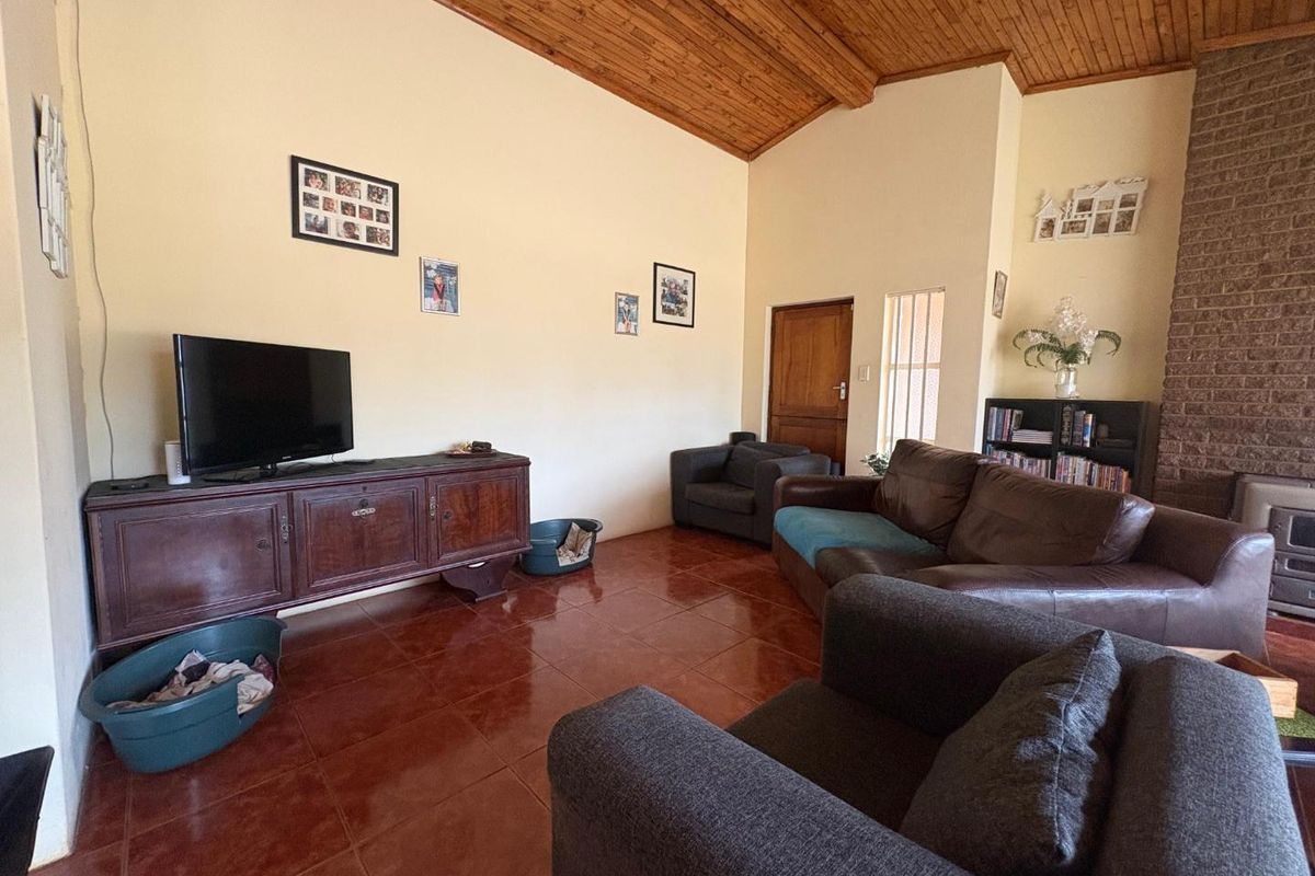 Spacious living room featuring high vaulted timber ceilings, tiled flooring, and a prominent brick fireplace, creating a warm and rustic atmosphere.