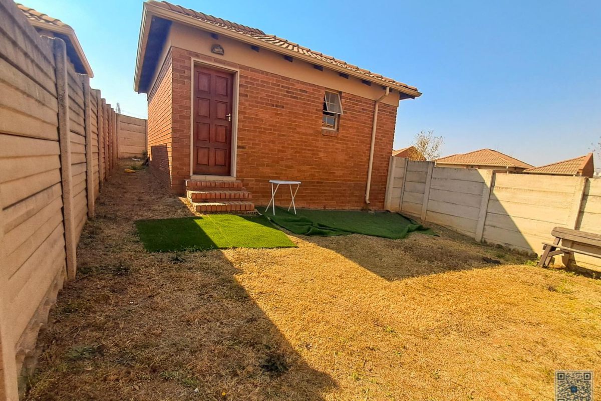 Rear view of a face brick outbuilding featuring a timber door, tiled roof, and enclosed by precast concrete boundary walls.