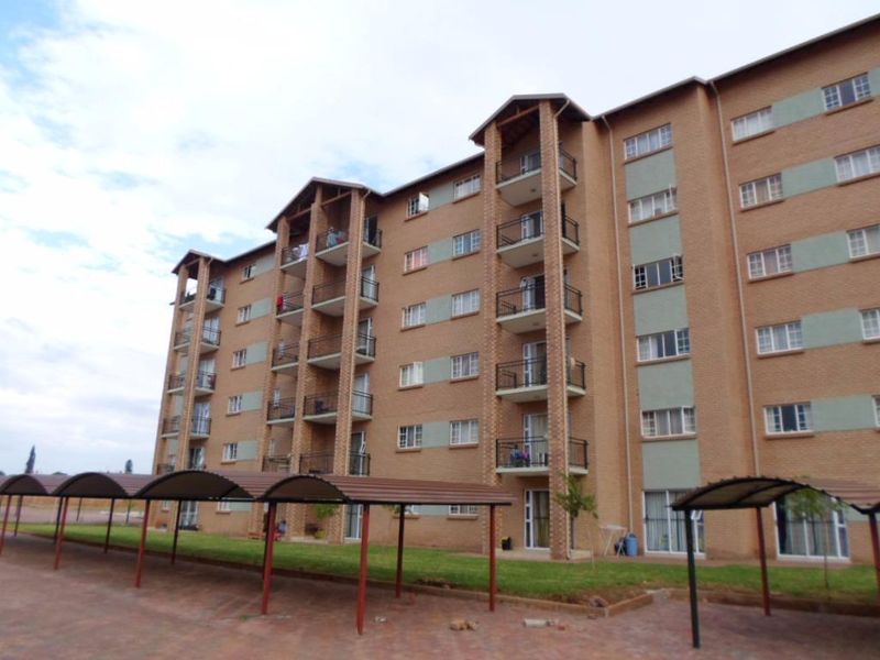 A multi-story brick apartment complex featuring private balconies, covered parking bays, and well-maintained surrounding lawn areas.