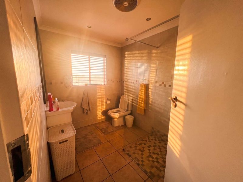 A functional bathroom featuring a walk-in shower with a glass screen, pedestal basin, and toilet, finished with neutral wall and floor tiling.