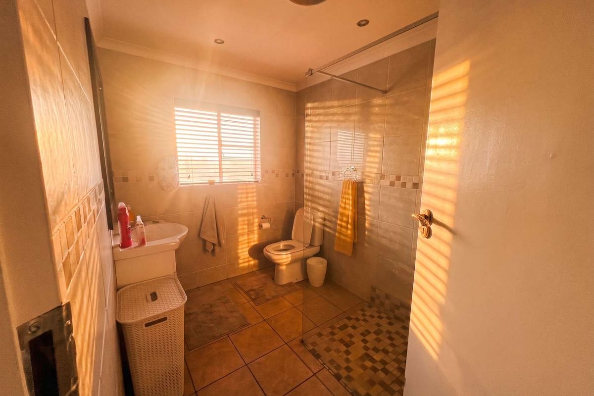 A functional bathroom featuring a walk-in shower with a glass screen, pedestal basin, and toilet, finished with neutral wall and floor tiling.