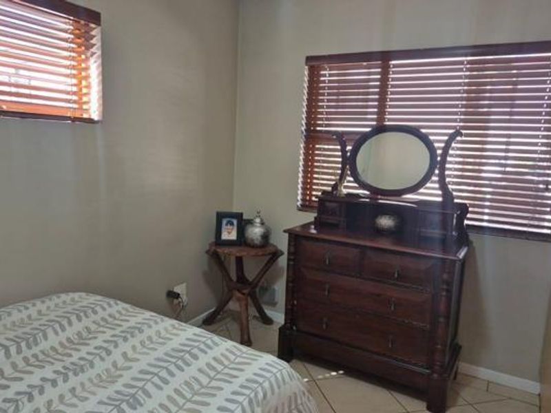 A bedroom featuring tiled flooring, neutral wall tones, and fitted venetian blinds on the windows.