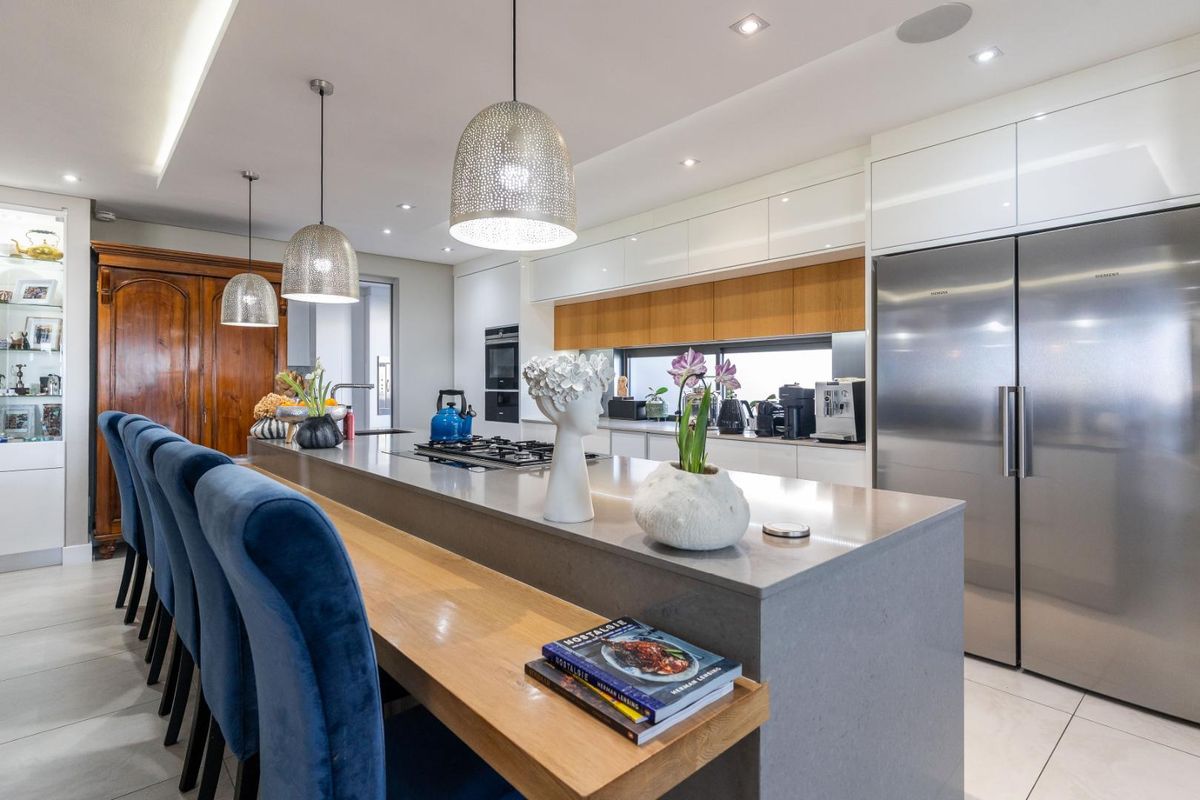 Modern kitchen featuring a large central island with stone countertops, integrated stainless steel appliances, sleek cabinetry, and contemporary pendant lighting.