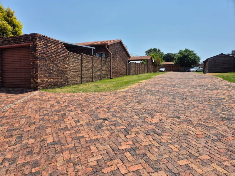 A view of the complex driveway featuring brick paving, face brick townhouse exteriors, and garage access.