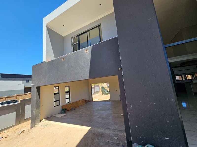 Rear view of a modern double-story house featuring a covered patio, tiled flooring, and balcony, currently in an unfinished construction state.