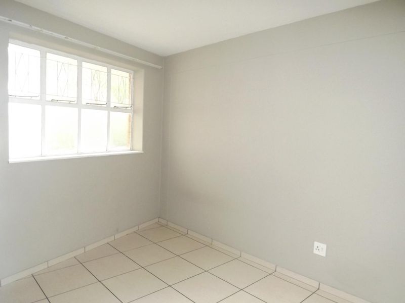 An empty bedroom featuring neutral tiled flooring, a window with security bars, and plain painted walls, offering a blank canvas for personalization.
