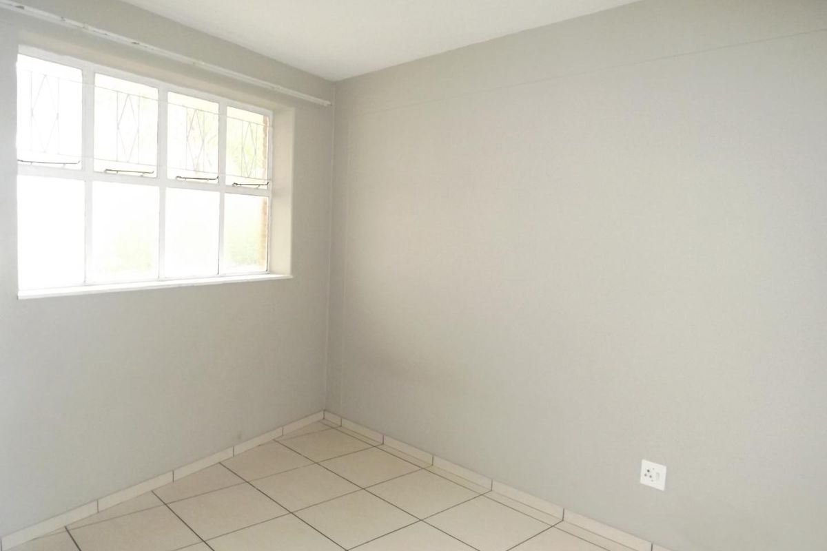 An empty bedroom featuring neutral tiled flooring, a window with security bars, and plain painted walls, offering a blank canvas for personalization.