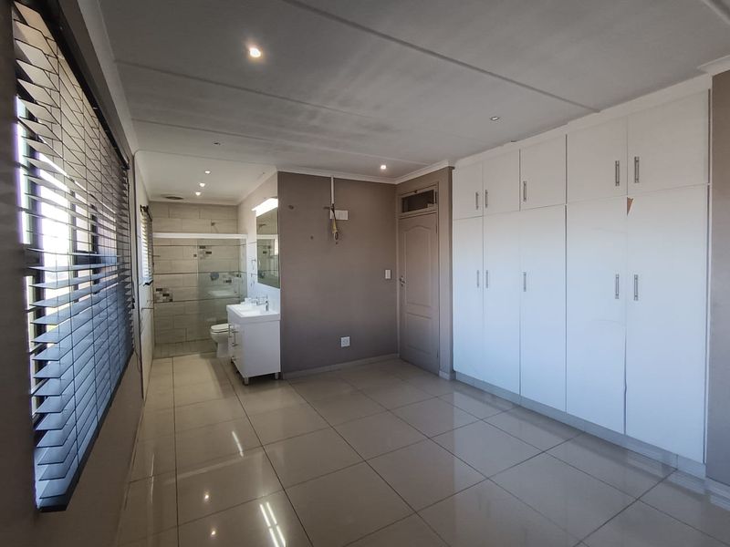 Spacious bedroom featuring tiled floors, extensive built-in cupboards, and an open-plan en-suite bathroom with a modern vanity and glass shower enclosure.