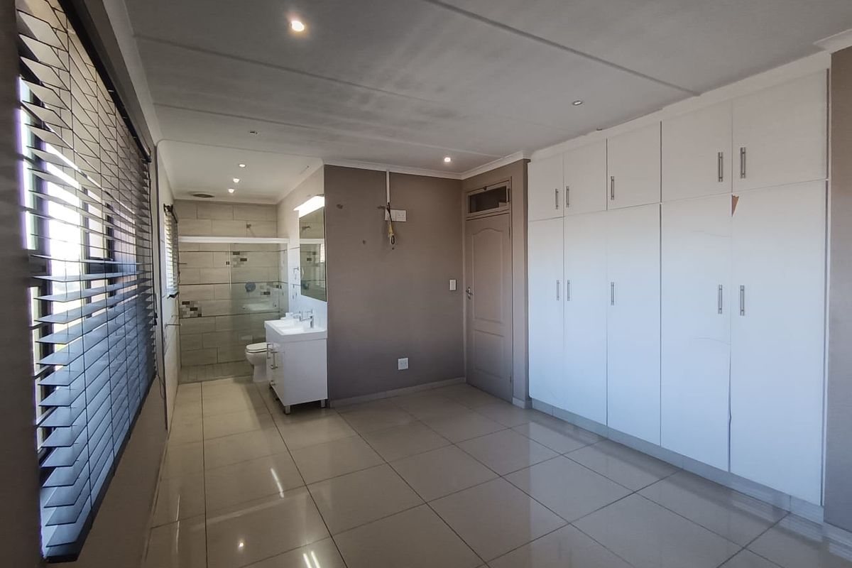 Spacious bedroom featuring tiled floors, extensive built-in cupboards, and an open-plan en-suite bathroom with a modern vanity and glass shower enclosure.