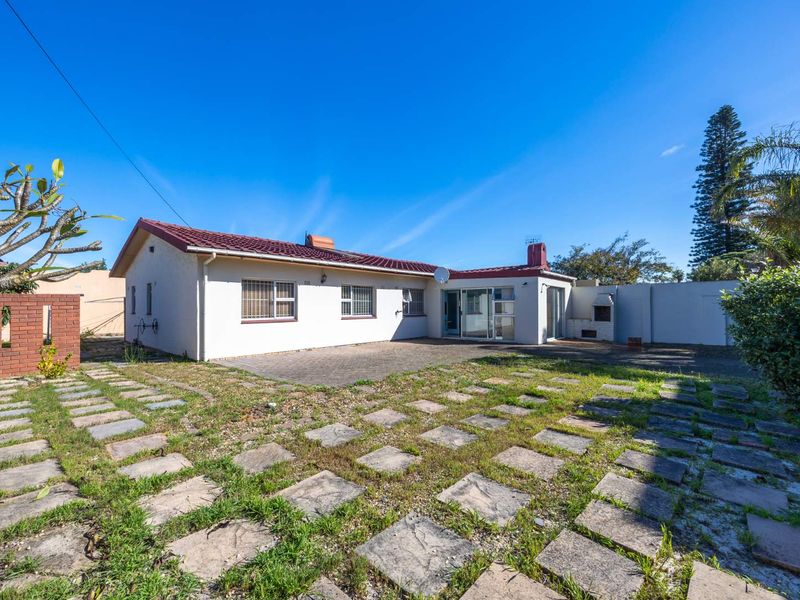 Rear view of the property featuring a paved patio area, built-in braai, and access to the home via sliding glass doors.