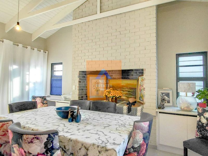 Spacious living area featuring a vaulted ceiling with exposed rafters and a prominent painted brick fireplace, creating a bright and airy atmosphere.