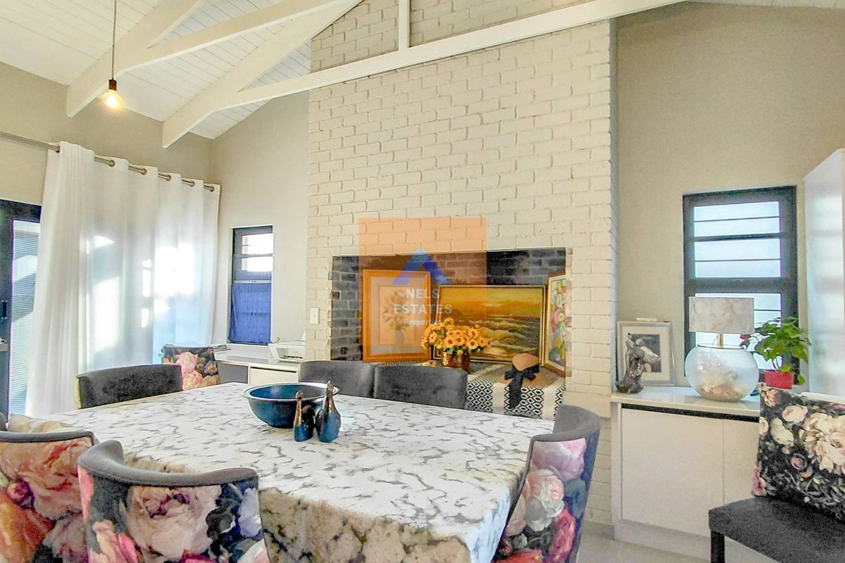 Spacious living area featuring a vaulted ceiling with exposed rafters and a prominent painted brick fireplace, creating a bright and airy atmosphere.