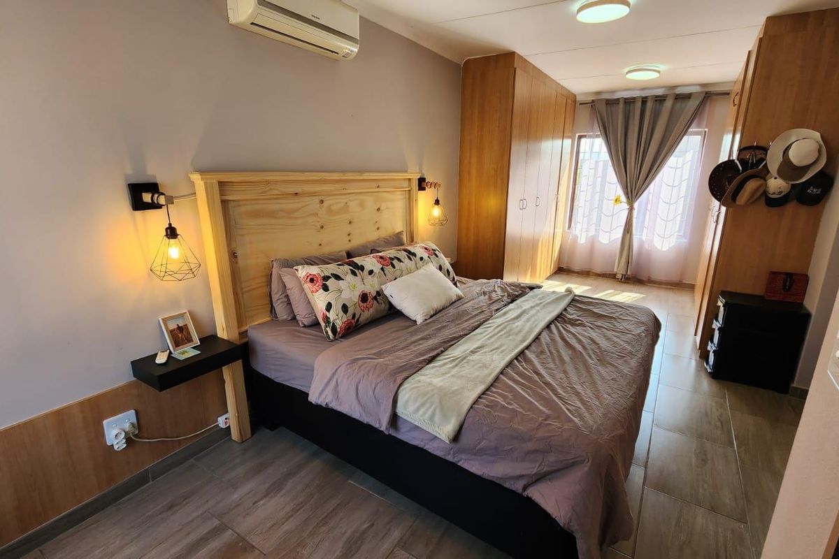 A well-maintained bedroom featuring built-in wooden cupboards, tiled flooring, and a wall-mounted air conditioning unit for climate control.