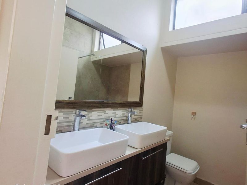 Modern bathroom featuring a double vanity with vessel sinks, tiled splashback, large mirror, and a toilet with high-level clerestory window for natural light.