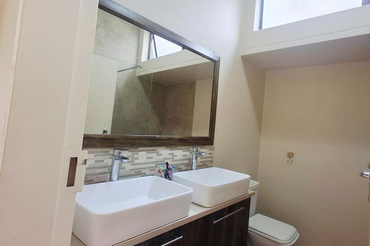 Modern bathroom featuring a double vanity with vessel sinks, tiled splashback, large mirror, and a toilet with high-level clerestory window for natural light.