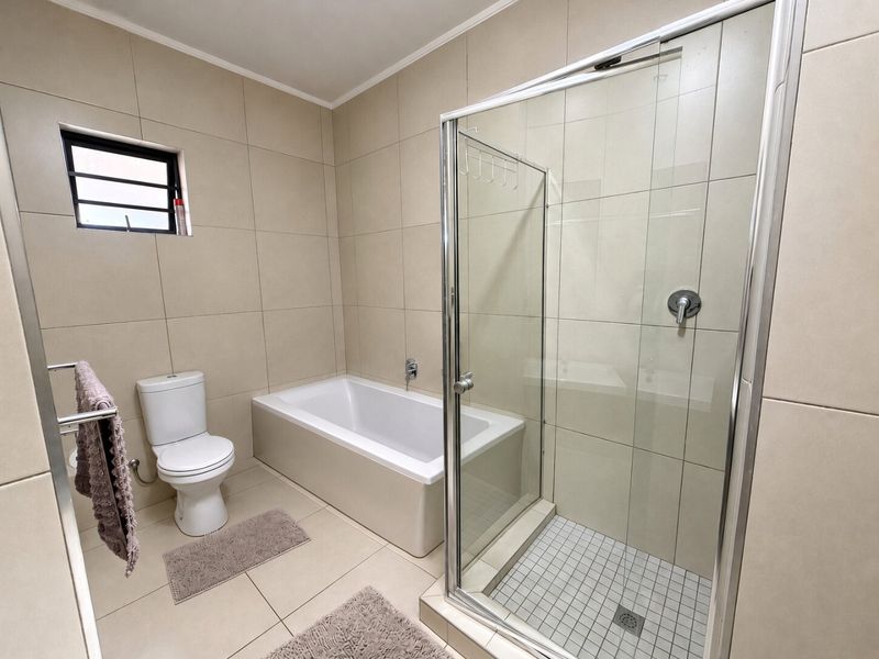 A clean, modern bathroom featuring a built-in bathtub, a separate glass-enclosed shower, and neutral floor-to-ceiling tiling.