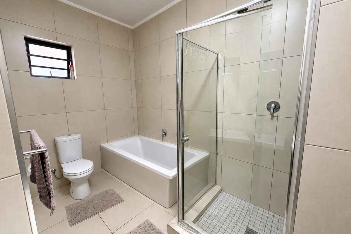 A clean, modern bathroom featuring a built-in bathtub, a separate glass-enclosed shower, and neutral floor-to-ceiling tiling.
